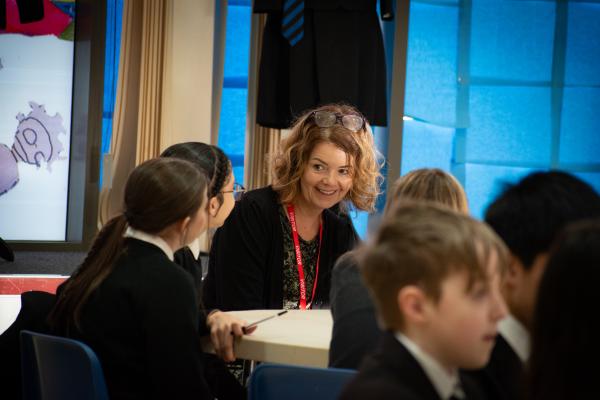 Photo of one of our professionals laughing with a group of students sat around a table. You can't see the student faces in the photo. The event took place in our assembly hall.