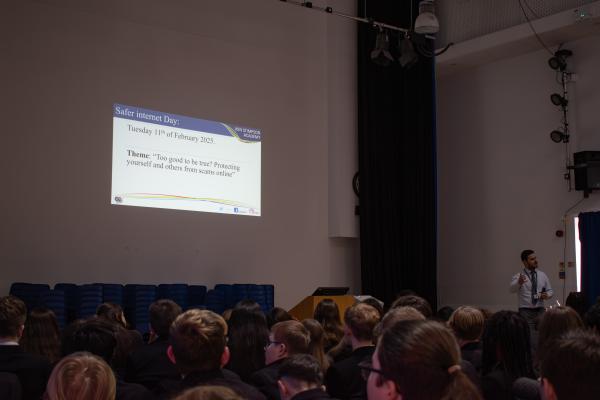 Image showing Mr Satari stood in front of a group of students talking them through a slide projected on the wall detailing safer internet day.