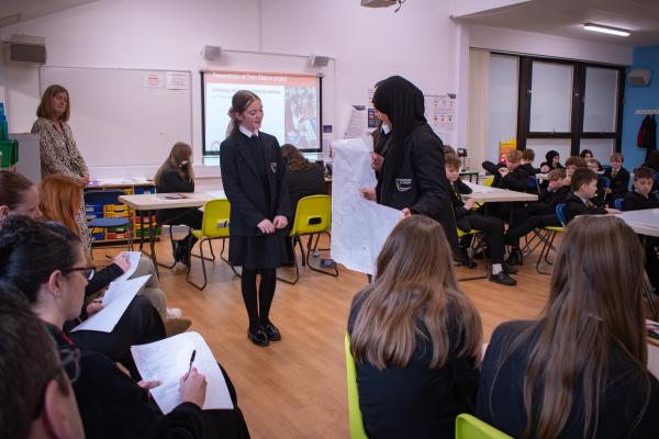 A group of students stand in front of a panel of Network Rail employees presenting their ideas for a railway station that meets the scenario they have been given.